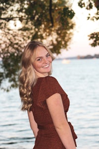 a woman in a brown dress standing near a body of water