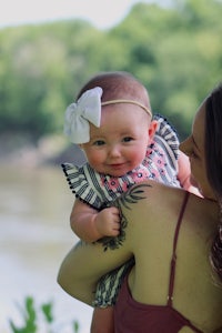 a woman holding a baby in front of a river