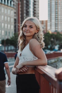 a blonde woman leaning on a railing in front of a city