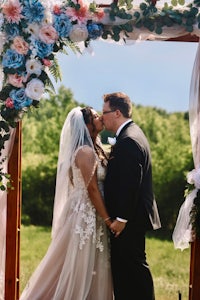 a bride and groom kiss under a blue and white wedding arch