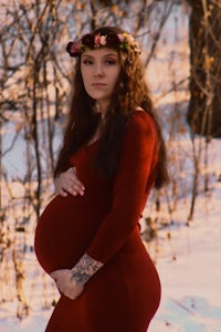 a pregnant woman in a red dress standing in the snow