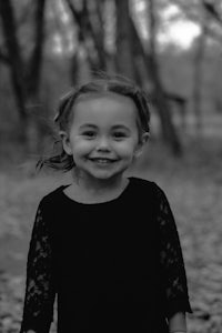 a black and white photo of a little girl standing in the woods