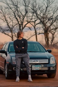 a man standing next to a black car on a dirt road