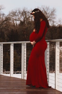 a pregnant woman in a red dress standing on a deck