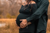 a pregnant man and woman hugging in front of a field