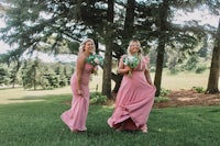 two bridesmaids in pink dresses standing in the grass