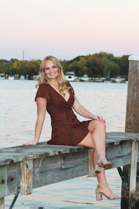 a young woman sitting on a dock in a brown dress