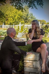 a man is kneeling on a stone wall to propose to a woman